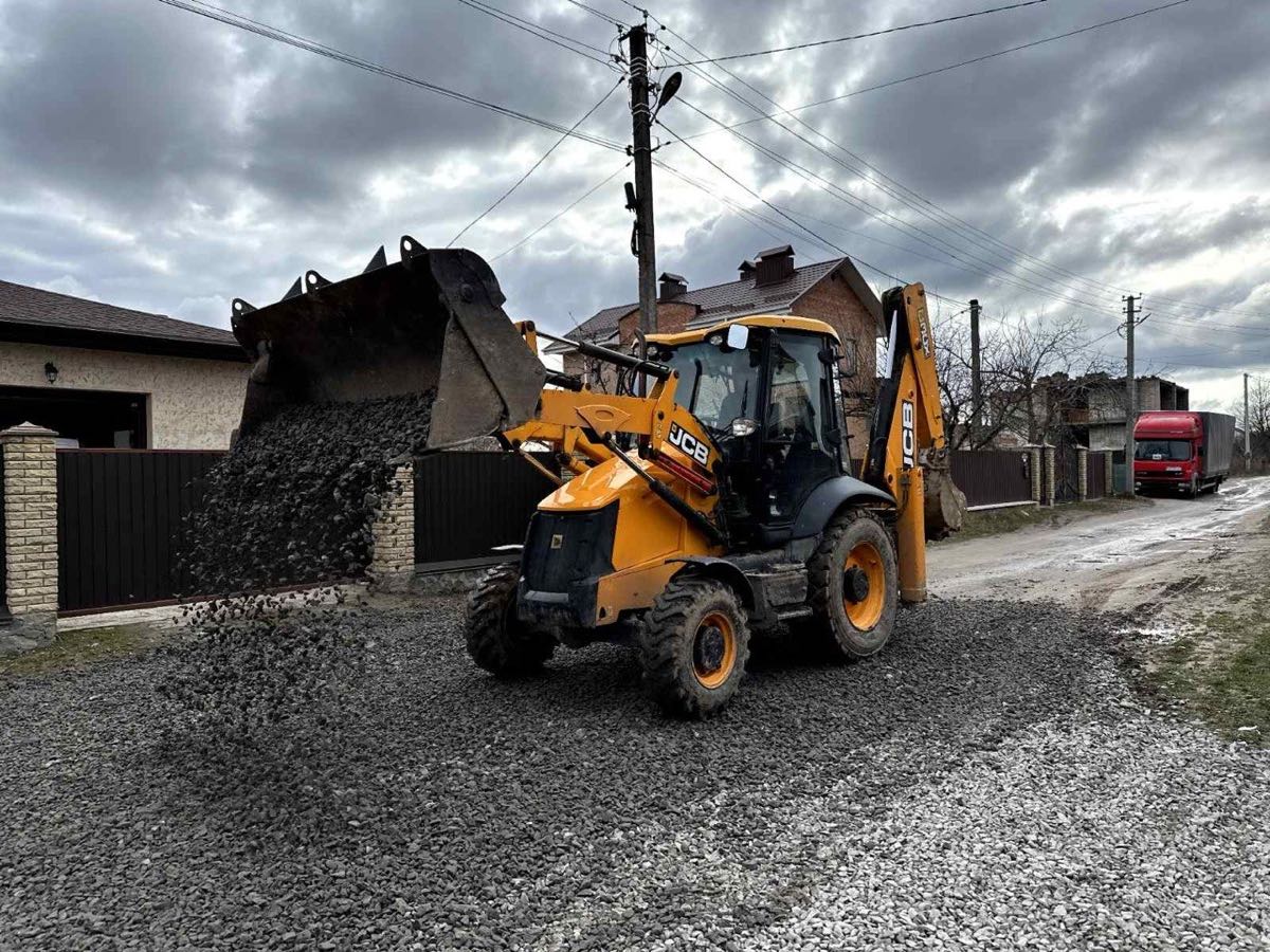 Екскаватор JCB 3CX розсипає щебінь на під'їзді до приватного будинку у Вінниці