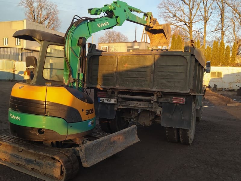 Мініекскаватор Kubota висипає ківш ґрунту в кузов самоскида