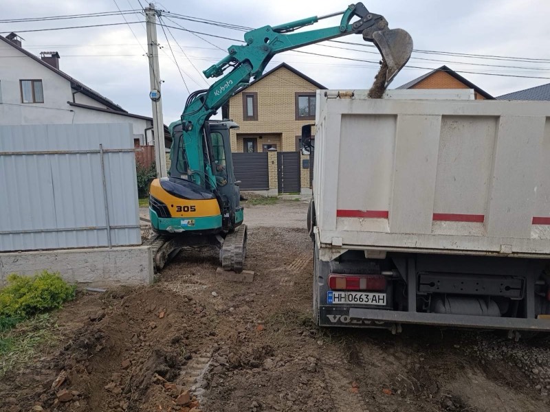 Мініекскаватор Kubota RX-305 вантажить ґрунт у самоскид Volvo біля приватного будинку