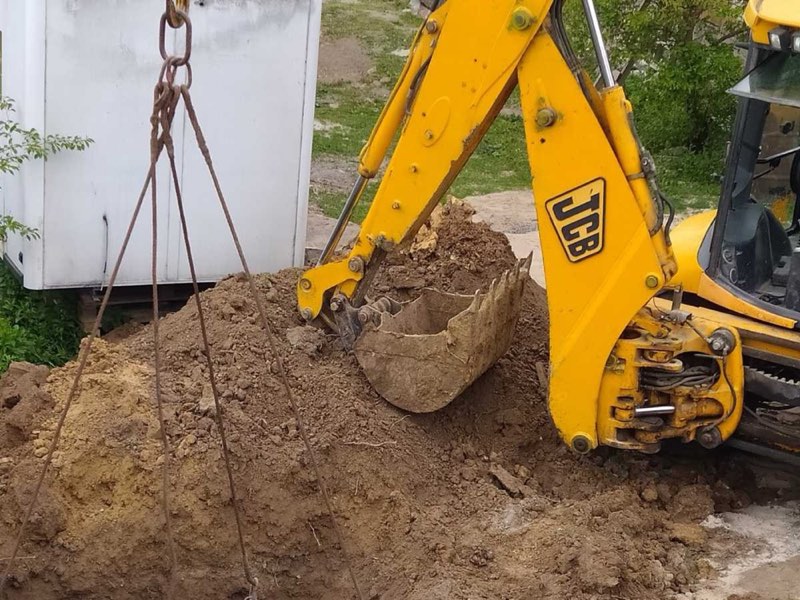 Екскаватор JCB опускає бетонне кільце в яму на подвір'ї