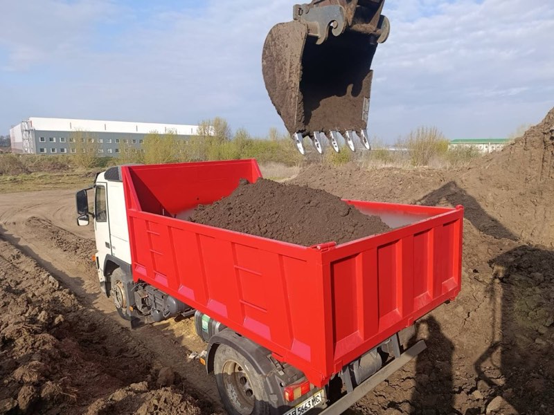 Ківш екскаватора над самоскидом із червоним кузовом, повним ґрунту