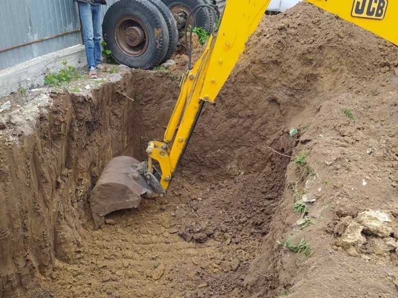 Ківш екскаватора JCB копає глибоку яму біля паркану